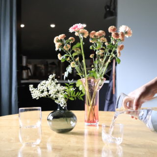 Vattenglas och vaser med blommor i på ett bord.